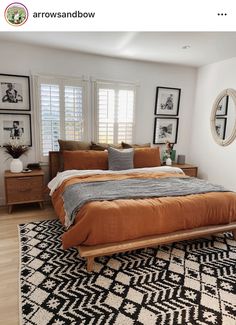 a bed with an orange comforter on top of it in a bedroom next to two windows