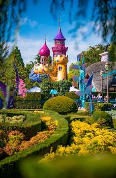 an elaborate garden with lots of flowers and plants in front of a castle shaped building