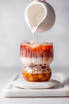 someone pours milk over the top of a dessert in a glass container on a white plate