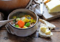 a bowl of soup next to some bread and butter on a wooden table with two spoons