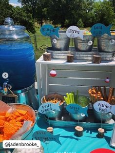 a table topped with buckets filled with food next to a blue cooler and sign