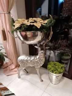 a silver vase sitting on top of a table next to a planter filled with flowers