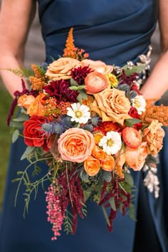 a woman in a blue dress holding a bouquet of orange and red flowers on her wedding day