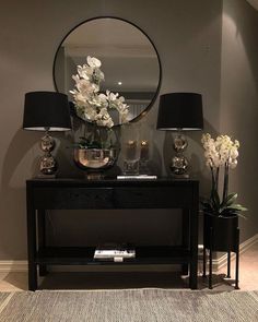 a black table topped with two lamps next to a mirror and vase filled with flowers