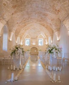 an indoor wedding venue with white flowers and candles on the aisle, along with tall vases