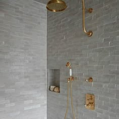 the shower head is connected to the wall in this modern bathroom with white brick walls and gold fixtures