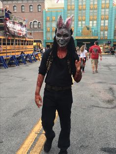 a man in an animal mask walks down the street with his hand up to the camera