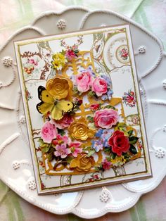 a white plate topped with a card and two butterflies on top of it, surrounded by flowers