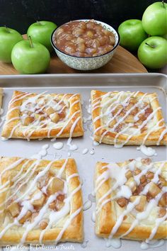 apples and cinnamon rolls with icing on a baking sheet next to bowls of apples