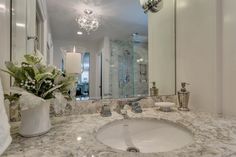 a bathroom with a marble counter top and white walls, along with a chandelier hanging from the ceiling