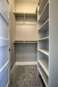 an empty walk in closet with white shelving and gray carpeting on the floor