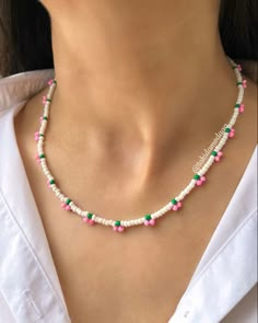 a woman wearing a necklace with pink, green and white beads on the front of her neck