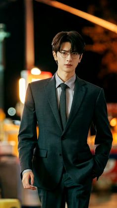 a man in a suit and tie standing on the street at night with his hands in his pockets