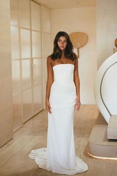 a woman in a white dress standing next to a sculpture and looking at the camera