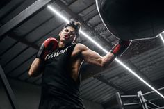 a man in black shirt and red boxing gloves standing next to punching bag with one hand