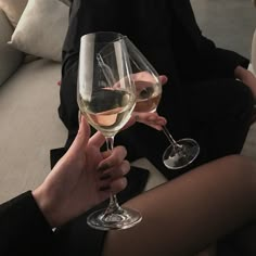 two people are holding wine glasses in their hands while sitting on a couch with white pillows