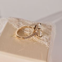 two wedding rings sitting on top of a white lace covered box with the ring in it's center