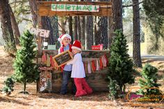 two children dressed up as santa and mrs claus standing in front of a christmas sign