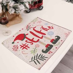 a table with a christmas themed placemat and wine glass on it next to a tree