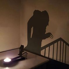 the shadow of a person standing on top of a stair case next to a lamp