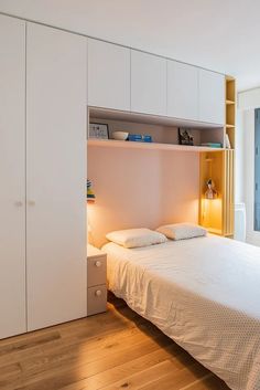 a bedroom with a bed, cupboards and shelves in the wall next to it