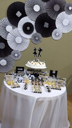 a white table topped with cake and cupcakes next to black and white paper fans