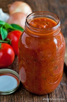 a jar filled with tomato sauce next to garlic, tomatoes and other fresh vegetables on a wooden table