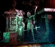 two statues are standing next to each other in front of a stone wall at night