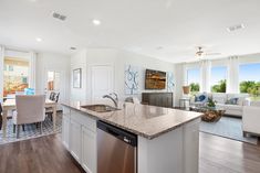 an open kitchen and living room area with hardwood floors, large windows, white walls, and stainless steel appliances