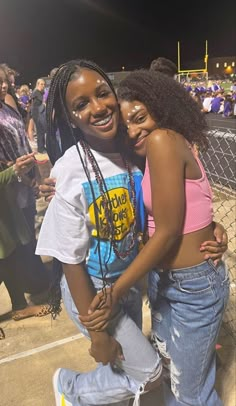 two young women hugging each other in front of a fence at a football game with people watching