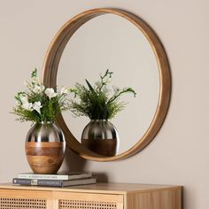 two vases with flowers are sitting on a wooden shelf in front of a round mirror