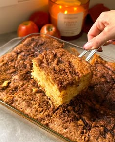 a person cutting into a piece of cake on top of a glass baking dish with apples in the background