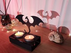 two candles sitting on top of a wooden table next to a bat shaped candle holder