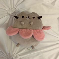 a stuffed animal with pink ears and wings on top of a white sheet covered bed