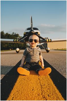 a baby sitting on the ground in front of an airplane