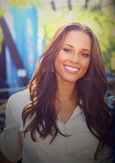 a woman with long brown hair smiling at the camera while standing in front of trees