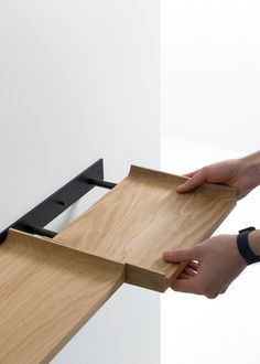 two hands are holding the edge of a wooden table with black metal brackets on it