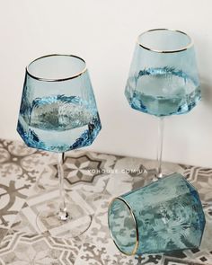 two blue wine glasses sitting next to each other on top of a patterned table cloth