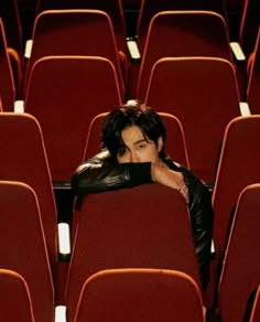 a man sitting in an empty auditorium with his head resting on the back of a red chair