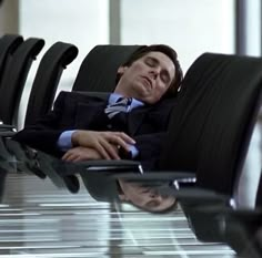 a man in a suit and tie laying on a chair with his head resting on the arm rest