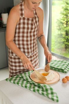 a woman in an apron preparing food on a wooden board with green and white checkered table cloth