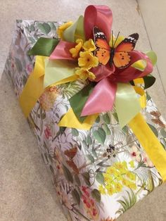 a gift wrapped in floral paper with a butterfly on top and yellow ribbon around it