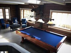 a pool table in the middle of a living room with chairs and lamps hanging from the ceiling