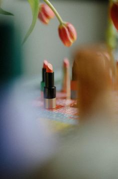 some lipsticks are laying on a table with tulips in the back ground