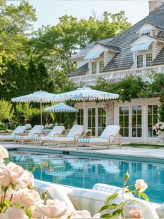 an outdoor swimming pool with chaise lounges and umbrellas next to the house