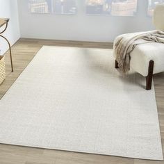 a white rug in a living room next to a chair and table with a blanket on it