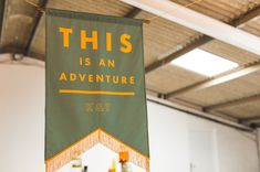 this is an adventure banner hanging from the ceiling in a room with white walls and wood beams