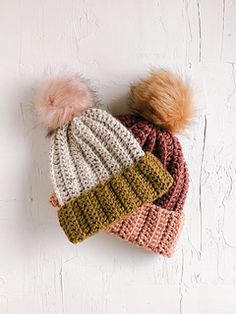 two crocheted hats with pom - poms on top