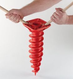 a man is holding two wooden sticks over a red object that looks like a spiral tube