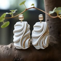 two white and gold earrings sitting on top of a tree branch